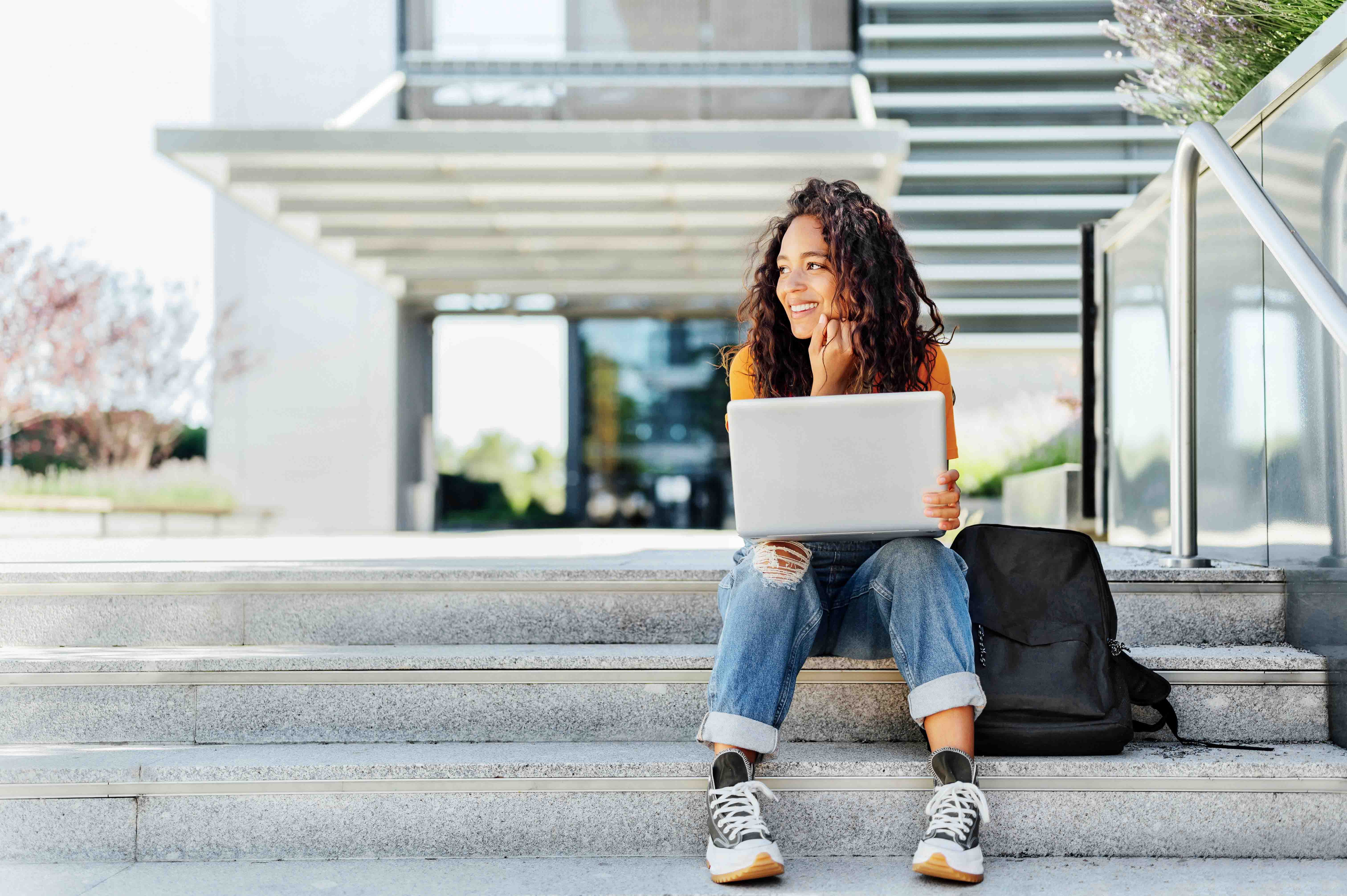 woman sitting on stairs outside of building with a laptop on her lap